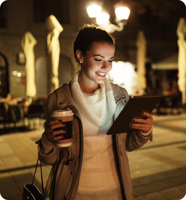Woman walking at night looking at tablet smiling